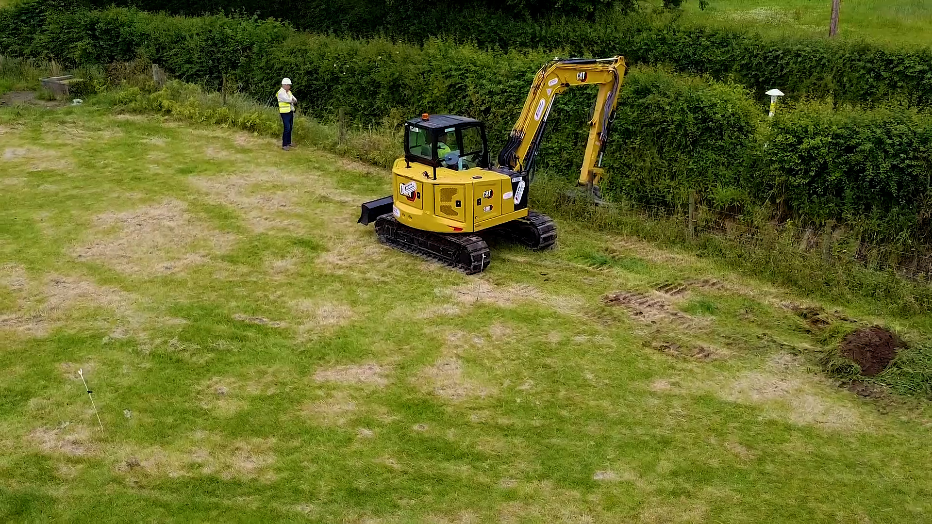 A yellow digger clearing a ditch close to a gas marker