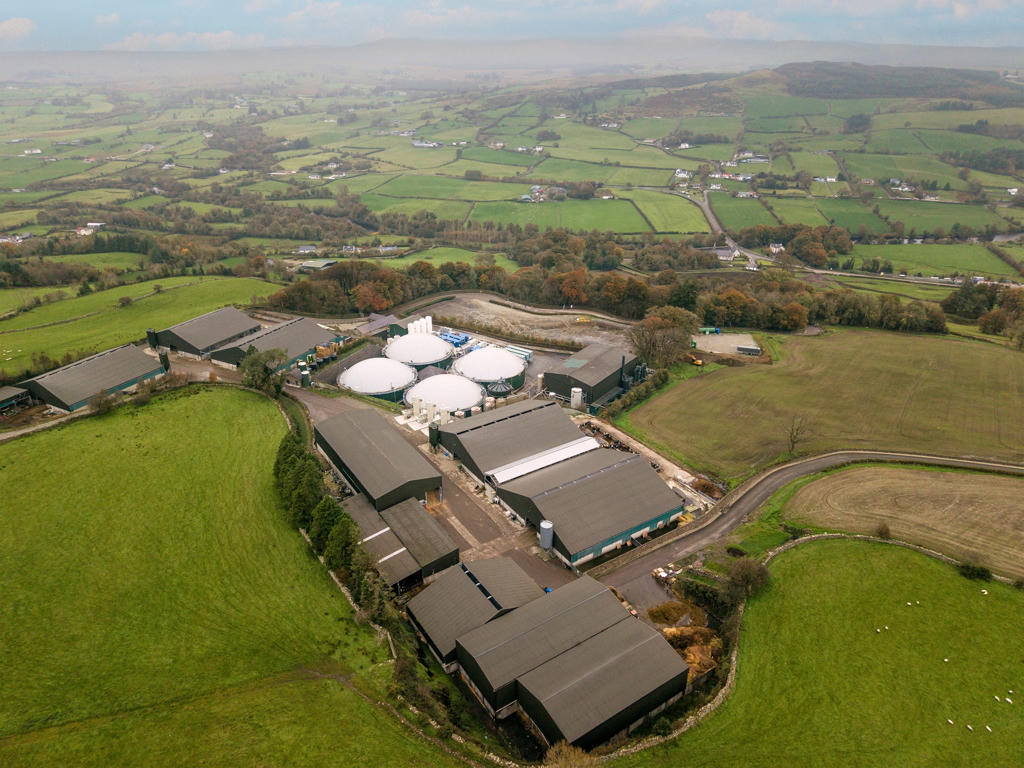 A drone shot of an AD plant supporting biomethane surrounded by fields and hills in the distance